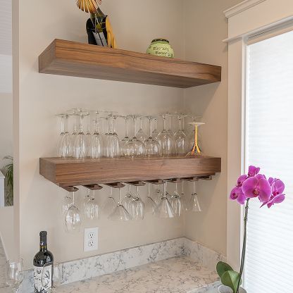 Wall-mounted wooden shelves holding stemware and decor above a marble countertop, with a purple orchid nearby