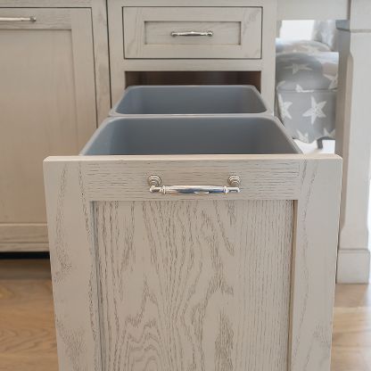 Light wood kitchen cabinet with two gray pull-out bins and a chrome handle