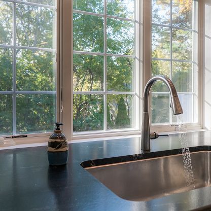 Kitchen sink by a window with trees outside, dark countertop, and soap dispenser nearby