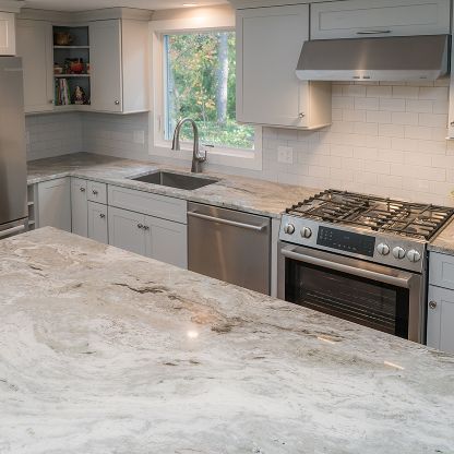 Modern white kitchen with marble island, stainless appliances, window, and tiled backsplash