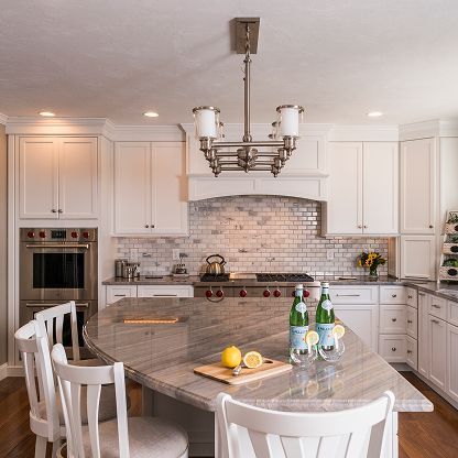 Bright white kitchen with marble island, bar stools, pendant light, and a tiled stove backsplash