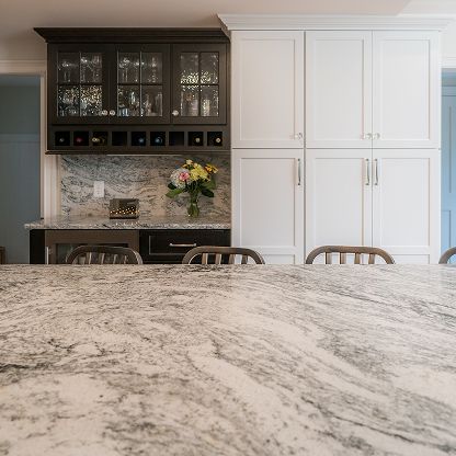 Modern kitchen with white cabinets, dark upper cabinets, granite island, and a small flower arrangement