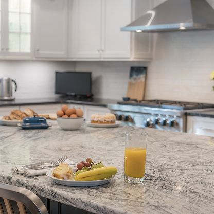 Bright modern kitchen with granite island holding breakfast, orange juice, and fruit plate