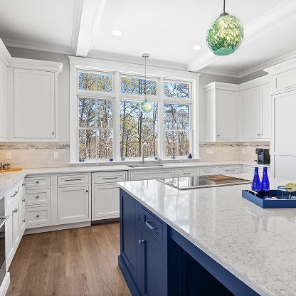 Bright modern kitchen with white cabinets, blue island, and large window over the sink