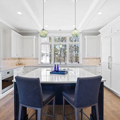 Bright white kitchen with large island, navy chairs, pendant lights, and big window.