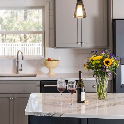 Bright kitchen with wine glasses, bottle, fruit bowl, and flowers on a marble island