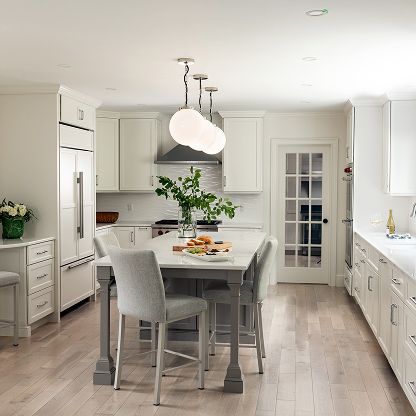 Bright modern kitchen with white cabinets, gray island, pendant lights, and a dining table with chairs