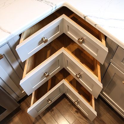Open kitchen corner cabinet with three white pull-out drawers and brass knobs, showing interior storage space.