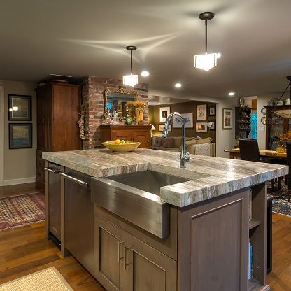 Modern kitchen with large marble island, stainless sink, wood cabinets, and warm recessed lighting