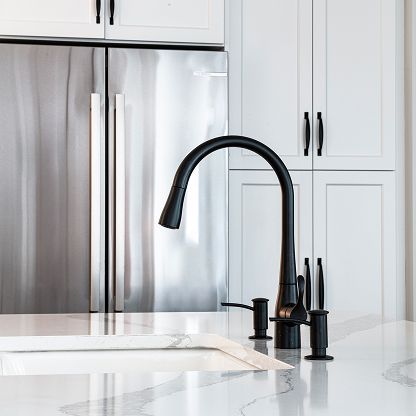 Modern kitchen sink with black faucet and white countertops in front of stainless steel refrigerator