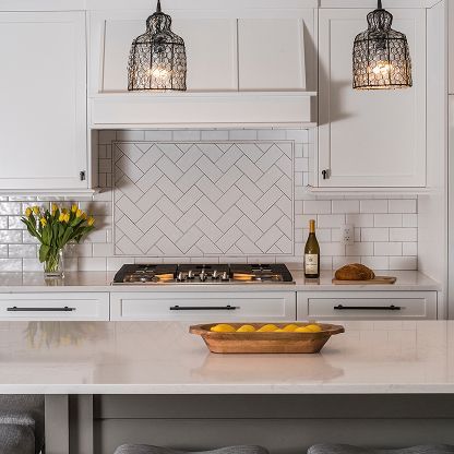 Bright white kitchen with patterned tile backsplash, pendant lights, and a vase of yellow flowers on the counter