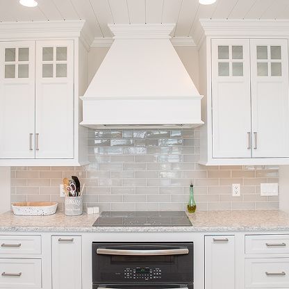 Bright white kitchen with gray backsplash, white cabinets, and stainless steel stove and range hood.
