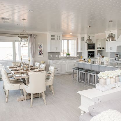 Bright white open-plan kitchen and dining room with farmhouse-style table, island stools, and pendant lights