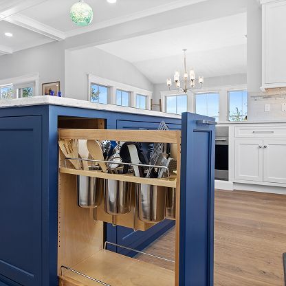Blue kitchen island with hanging pots in a bright white kitchen