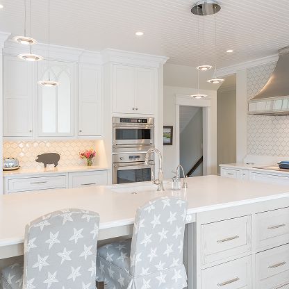 Bright white modern kitchen with large island, built-in ovens, and star-patterned bar stools.