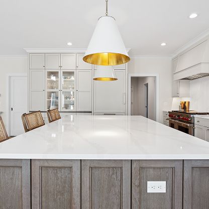 Bright white modern kitchen with gold pendant lights, large island, and gray lower cabinets