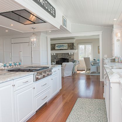 Bright white kitchen with wood floors, island, and open dining area leading to a living room.