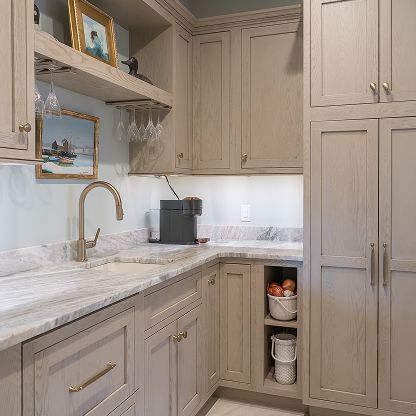 Light beige kitchen with marble counters, gold fixtures, open shelf decor, and built-in cabinets.