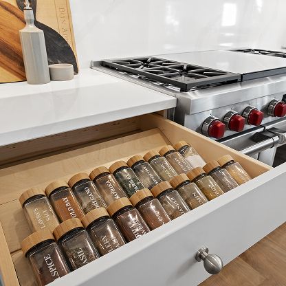 Open kitchen drawer neatly filled with glass spice jars beside a gas stove