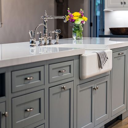 Modern gray kitchen island with a chrome faucet, white countertop, and a vase of colorful flowers