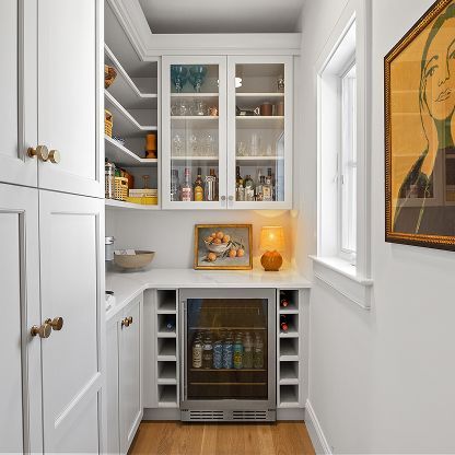 Bright white wet bar with glass cabinets, mini fridge, and warm lamp in a narrow alcove