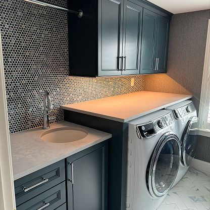 Compact laundry room with gray cabinets, sink, mosaic tile backsplash, and washer and dryer under a countertop
