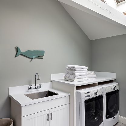 Small laundry room with sink, white cabinets, stacked towels, and a washer-dryer under a sloped ceiling.