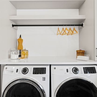 Laundry room with white shelves, hanging yellow hangers, and two front-loading washers below.