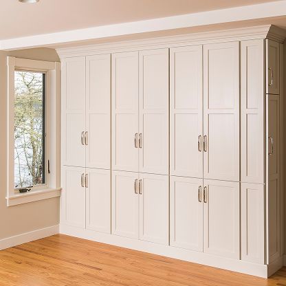 White built-in wardrobe cabinets with silver handles in a bright room beside a window.