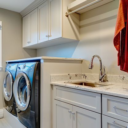Laundry room with front-loading washer and dryer beside a sink, white cabinets, and hanging clothes
