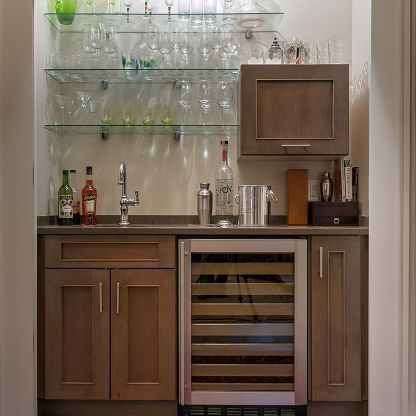 Modern bar cabinet with glass shelves, wine fridge, bottles, glasses, and sink in a wood-paneled room