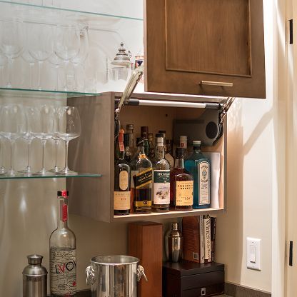 Open bar cabinet with liquor bottles and glassware beside a mirrored shelf of wine glasses