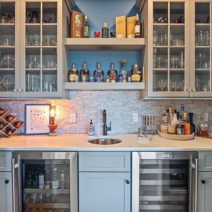 Stylish kitchen bar with glass cabinets, blue walls, wine bottles, sink, and undercounter fridge