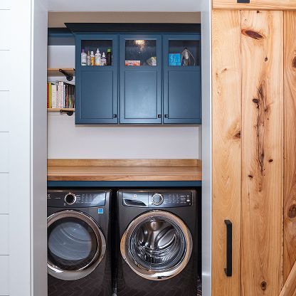 Laundry nook with blue cabinets, wood countertop, and two front-loading machines behind a sliding wood door