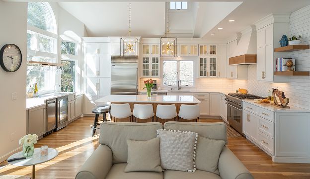 Bright modern kitchen with island, white cabinets, wood floors, and a sofa in the foreground