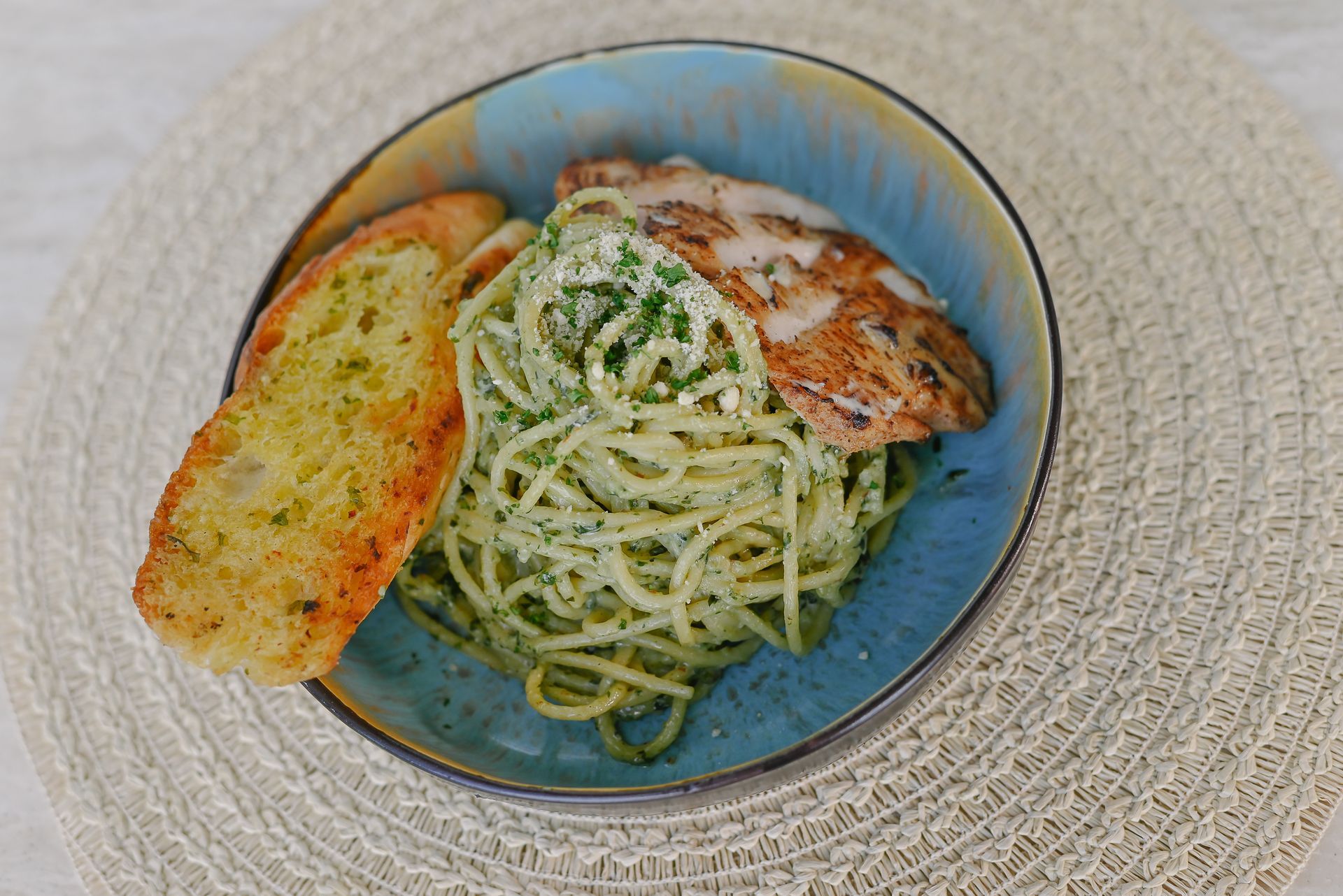 A bowl of spaghetti with chicken and garlic bread on a table.