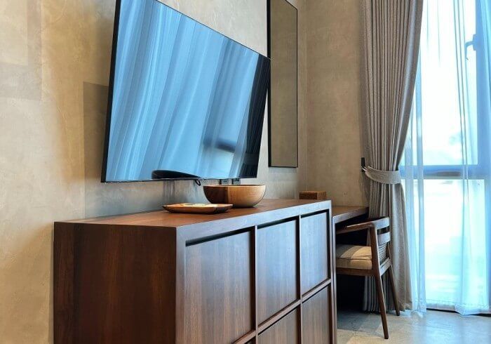 A flat screen tv is mounted on the wall above a wooden dresser.
