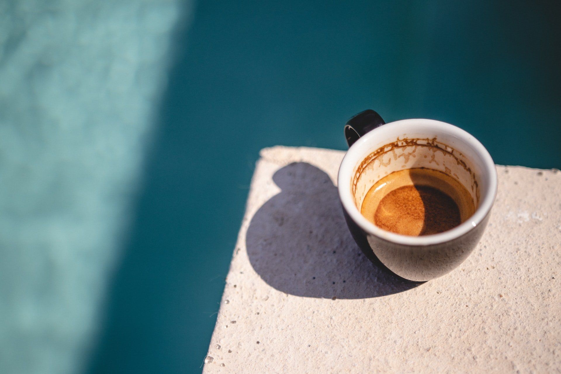 A cup of coffee is sitting on a table next to a pool.
