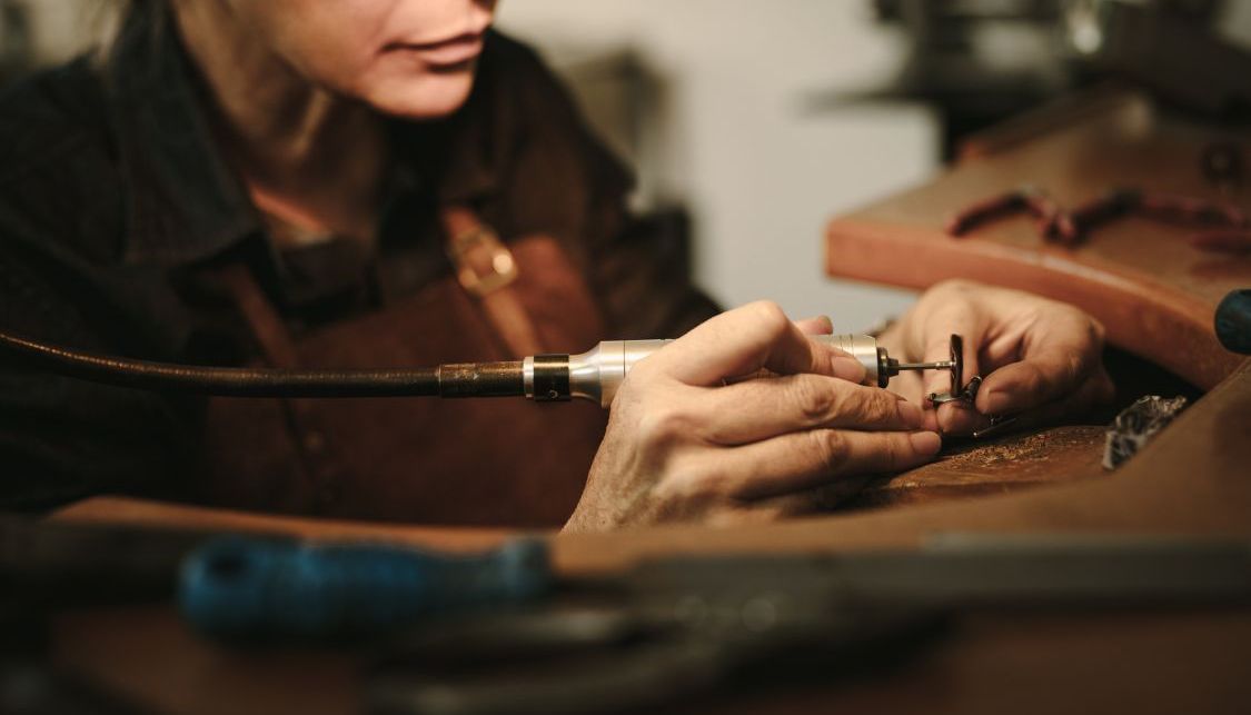 A woman is working on a piece of jewelry with a machine.