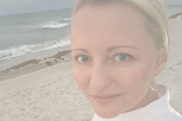 Close-up portrait of Martina Huppertová on a beach, with pale sand and ocean waves visible behind he