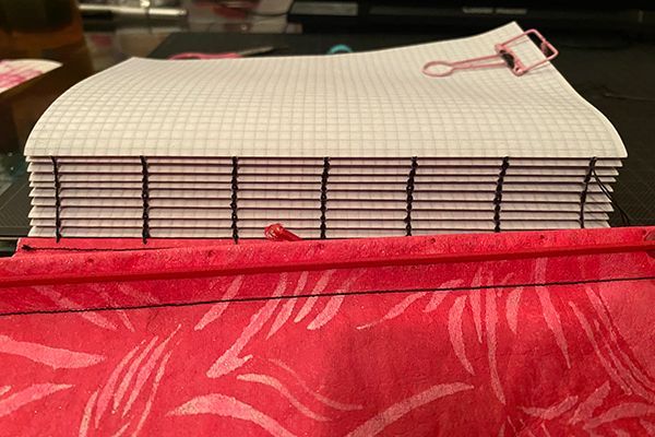     Handmade notebook with graph-paper pages sewn together with black thread above a red patterned cover.