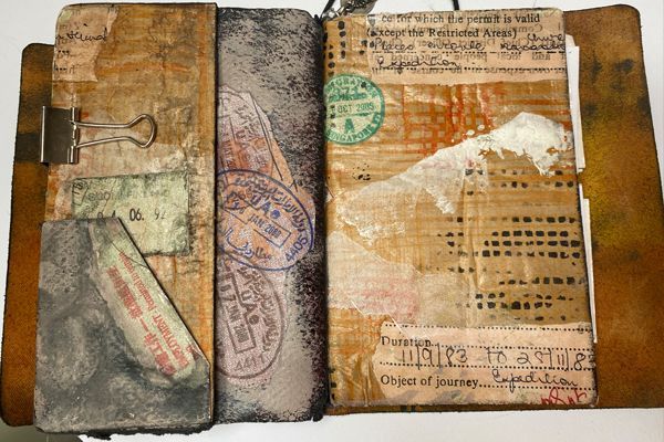    Open handmade travel notebook decorated with layered paper, passport stamps and handwritten journey details.