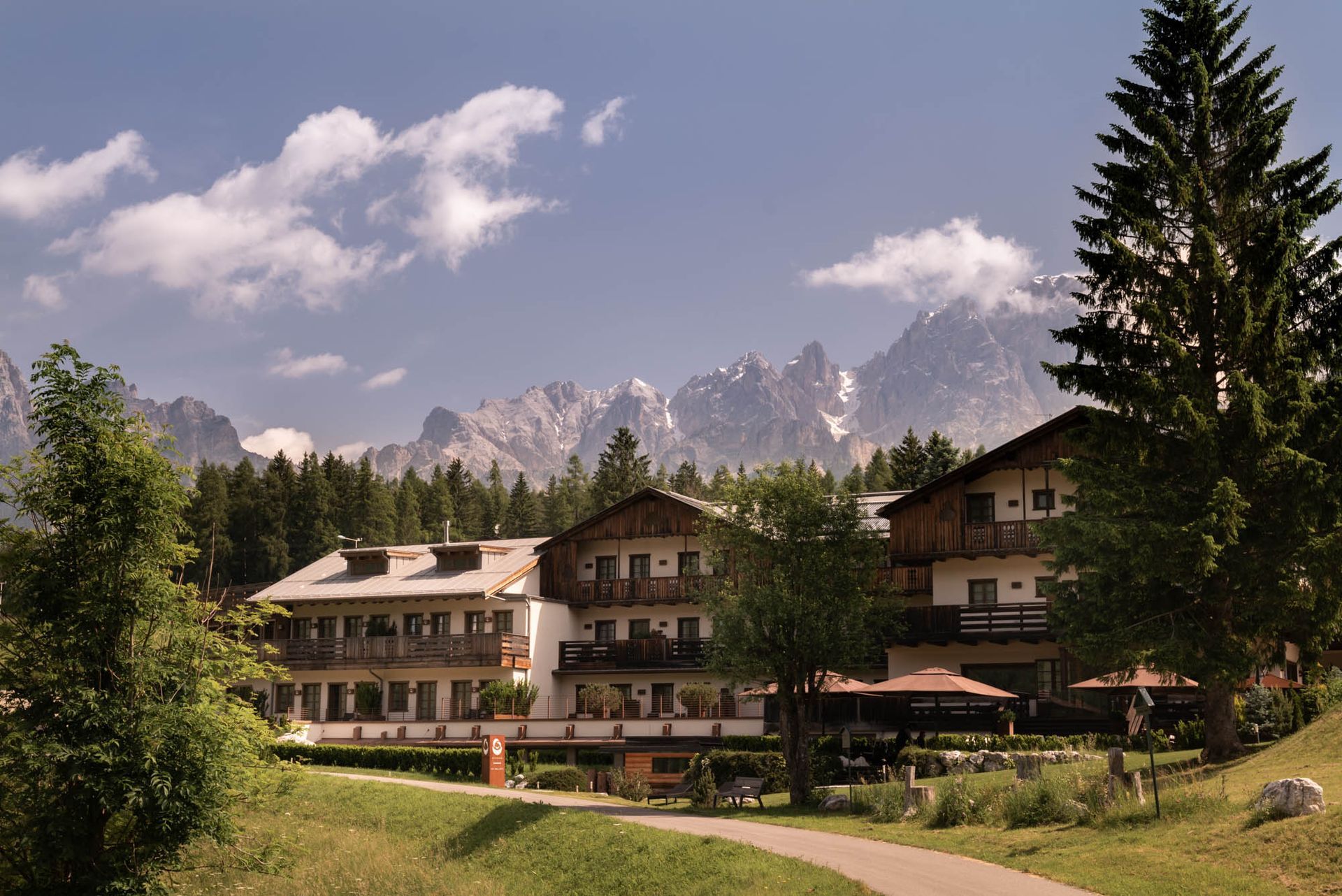 Rifugio di montagna con balconi in un prato verde, con cime frastagliate e un cielo azzurro sullo sfondo.