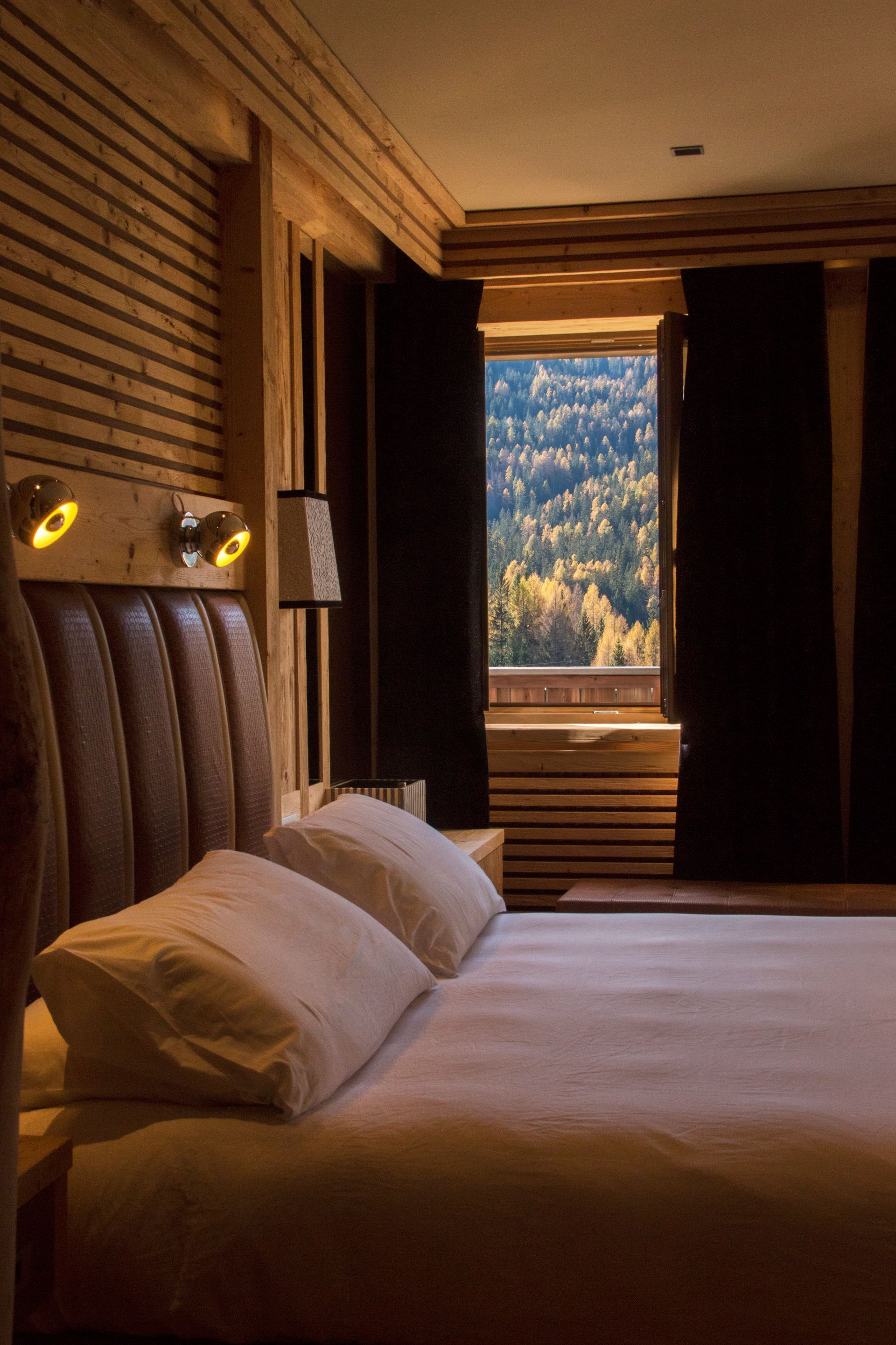 Cozy hotel bedroom with a bed and open window overlooking a forested mountain view