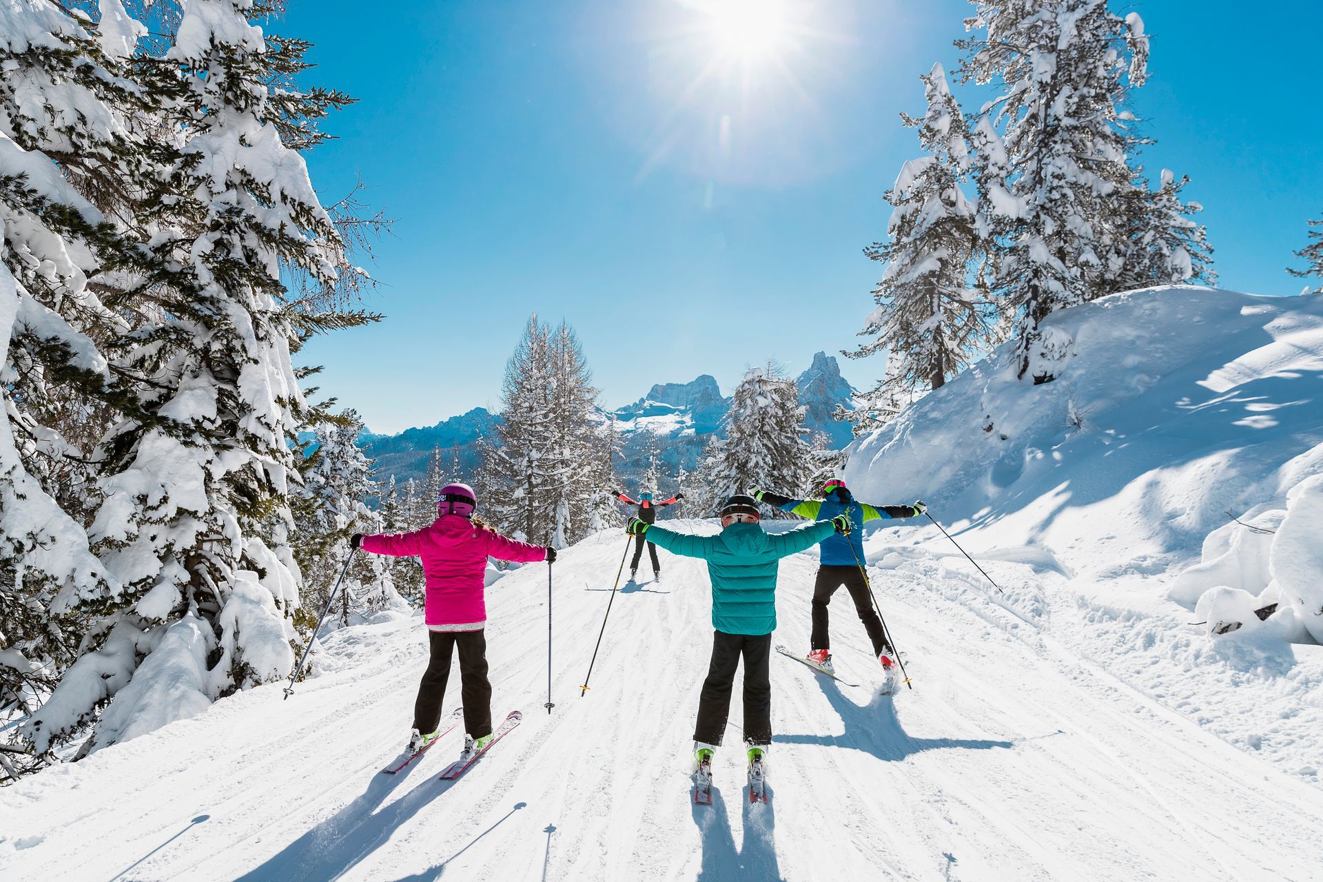 Tre sciatori con giacche colorate su un sentiero di montagna innevato sotto un sole splendente