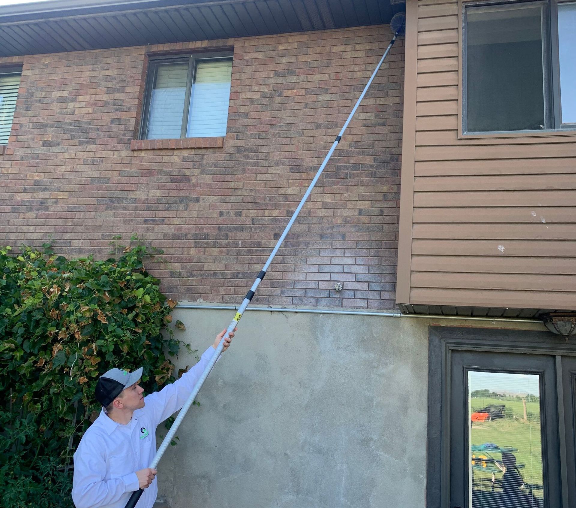 Pest control technician sweeping eaves of a home