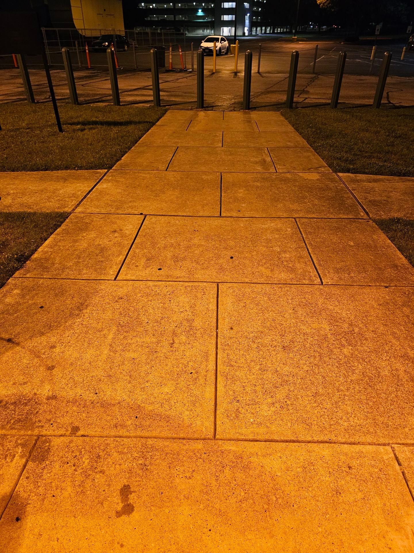 Orange-lit stone walkway leading to a fenced area at night with distant city lights