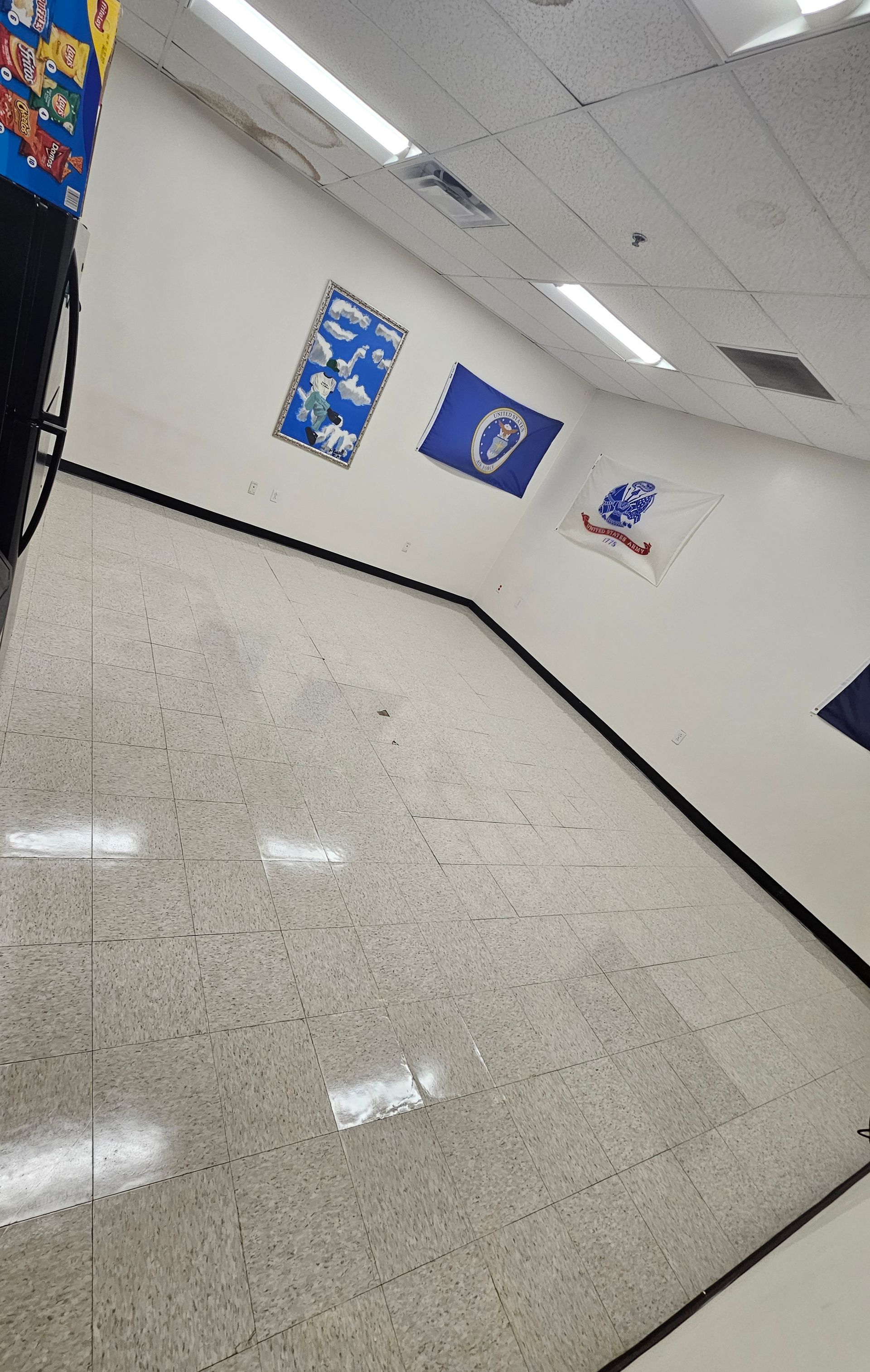 Empty school hallway with white walls, speckled floor, and blue wall posters, viewed at an angle.