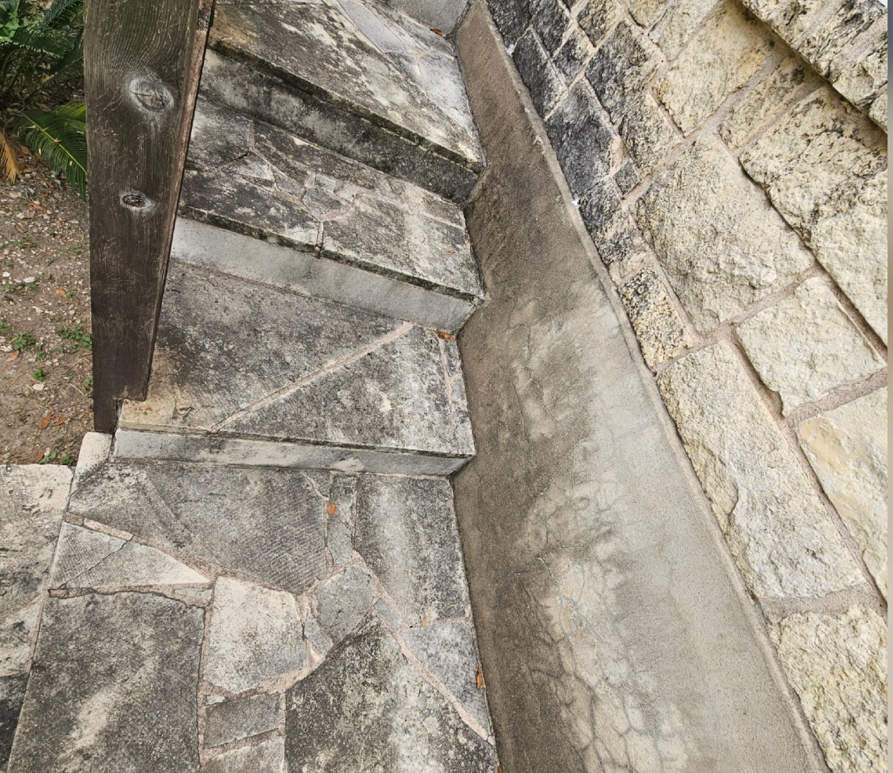 Narrow stone staircase beside a stone wall, with worn steps and a metal railing