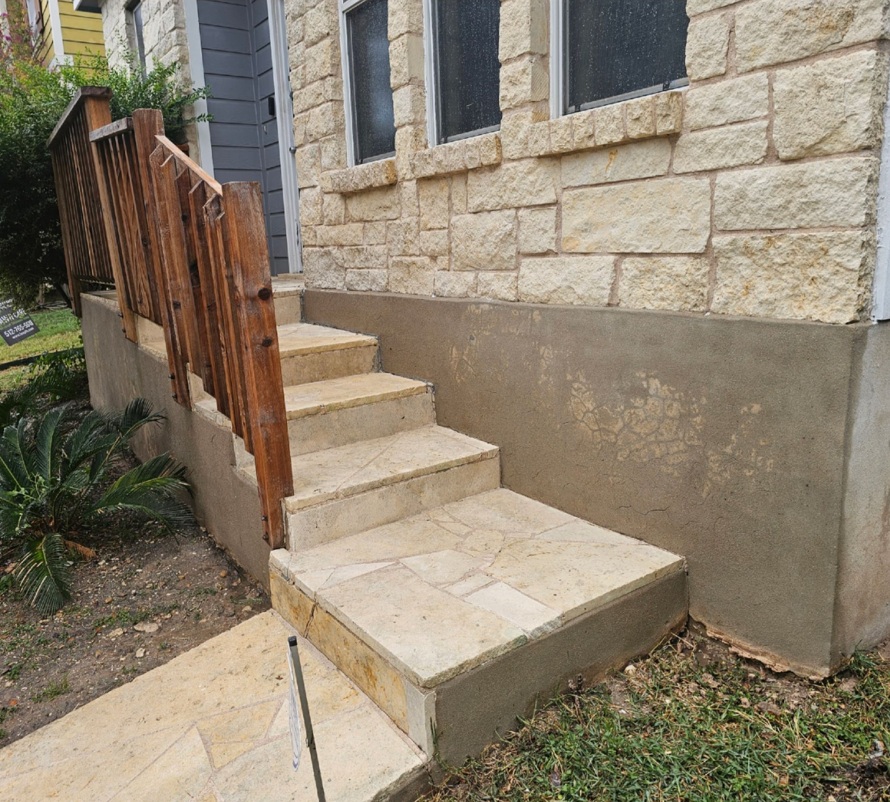 Stone steps and wooden railing leading to a house entrance with textured stone and gray walls